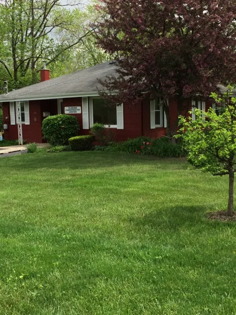 Florian Chiropractic: a single-story red building with white trim and a grey roof, set back behind a wide green lawn, with a purple-leaf tree in front.