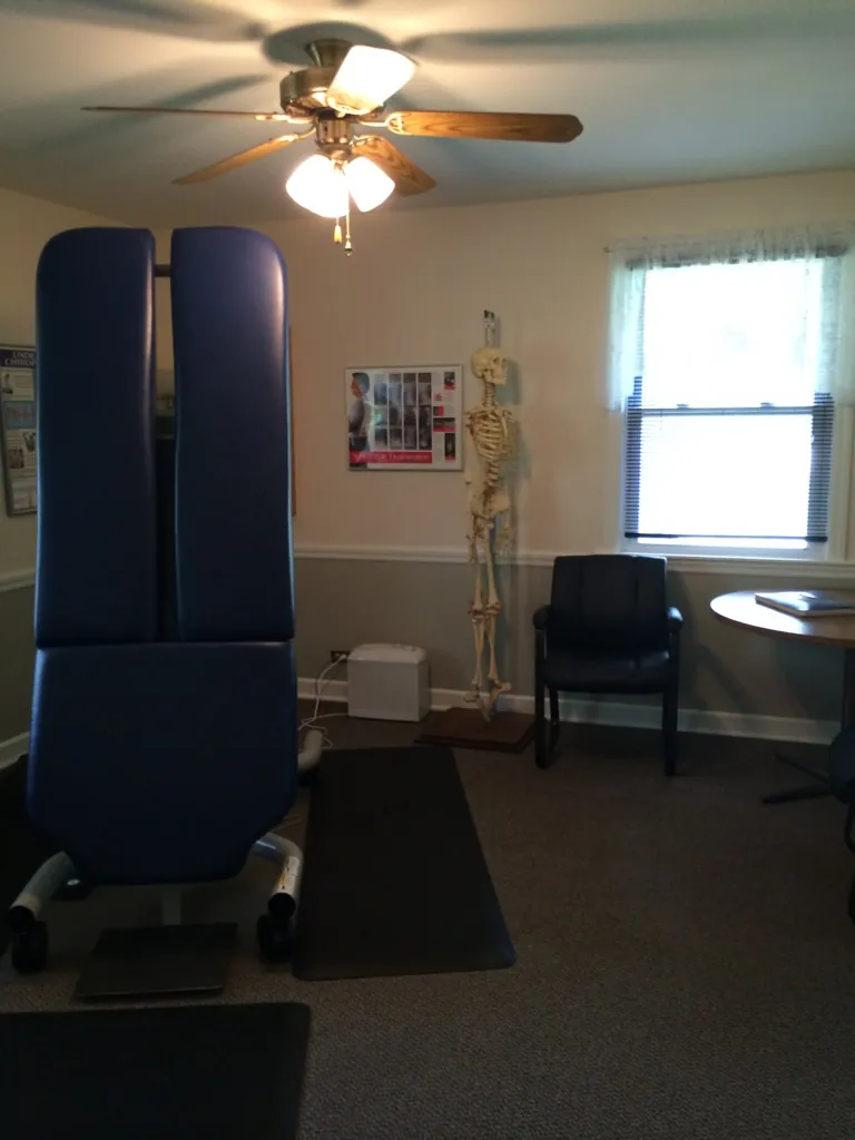The adjusting room: a navy chiropractic table, a model skeleton, a chair and a window.