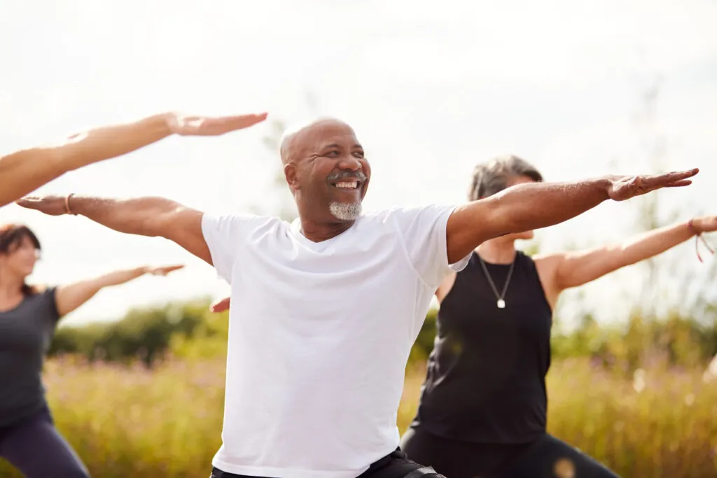 Smiling adults stretching their arms wide in an outdoor exercise class in a meadow.