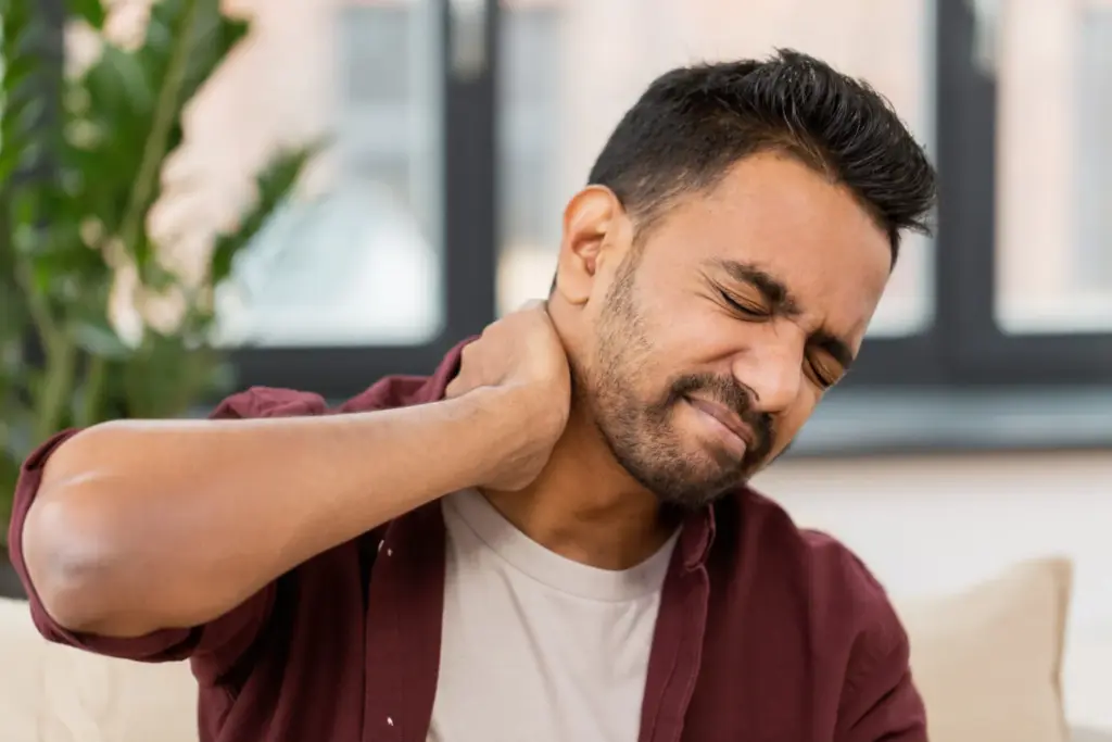 A man wincing and rubbing the back of his neck.