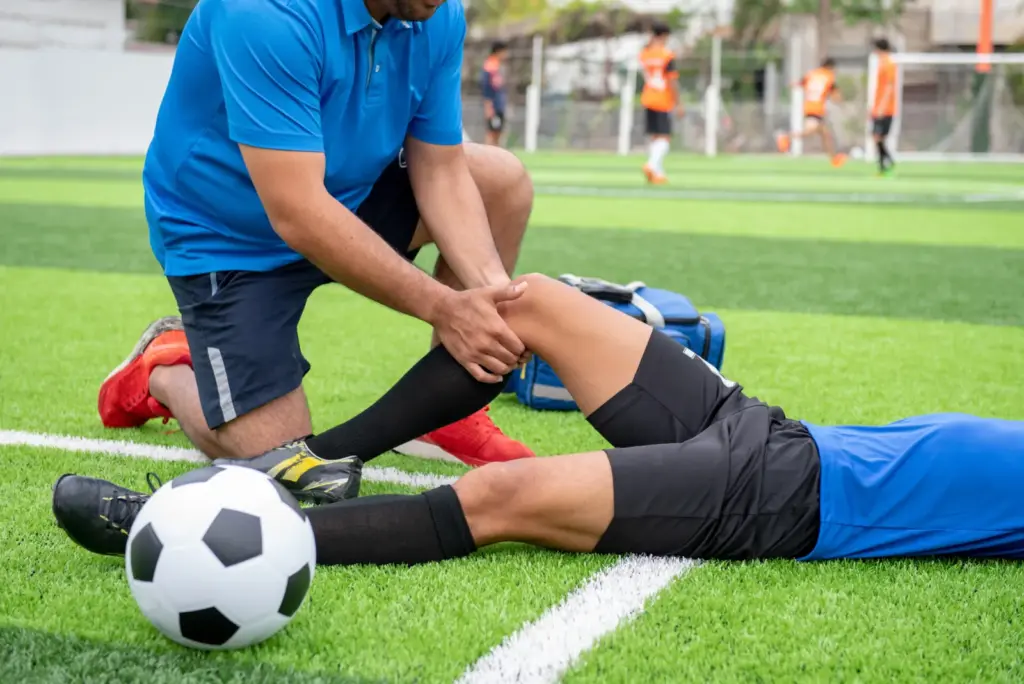 A trainer checking a soccer player’s leg on the field.