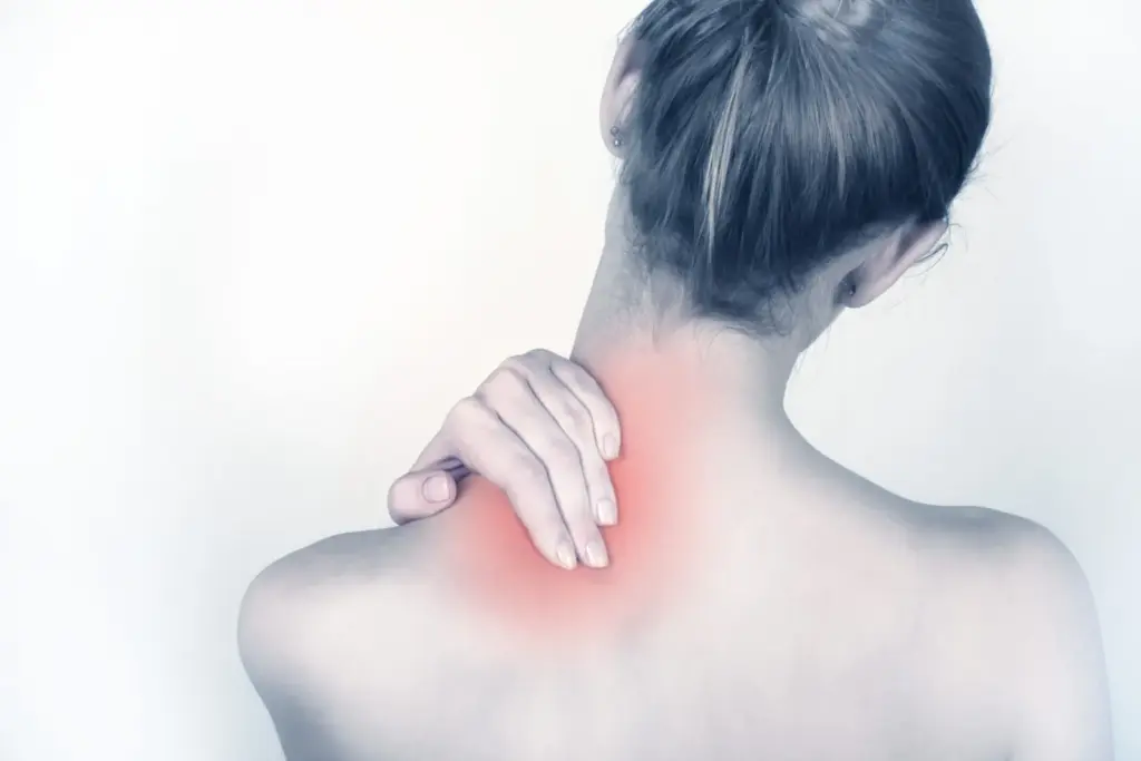 A woman holding the back of her neck where it meets the shoulder, the sore spot glowing red.