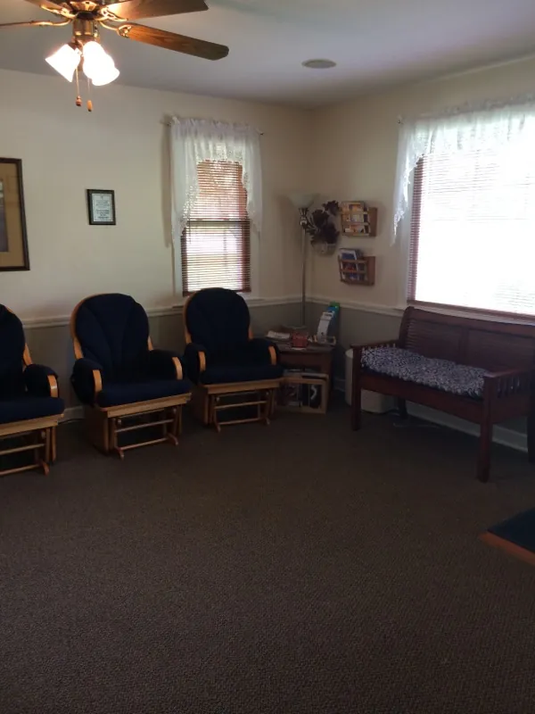 The waiting room: navy glider rocking chairs, a cushioned wooden bench and windows with lace curtains.